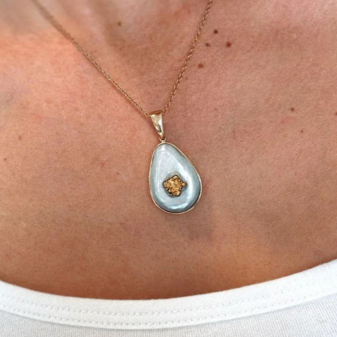 Teardrop-shaped pendant necklace with a gold chain on a person wearing a white top.